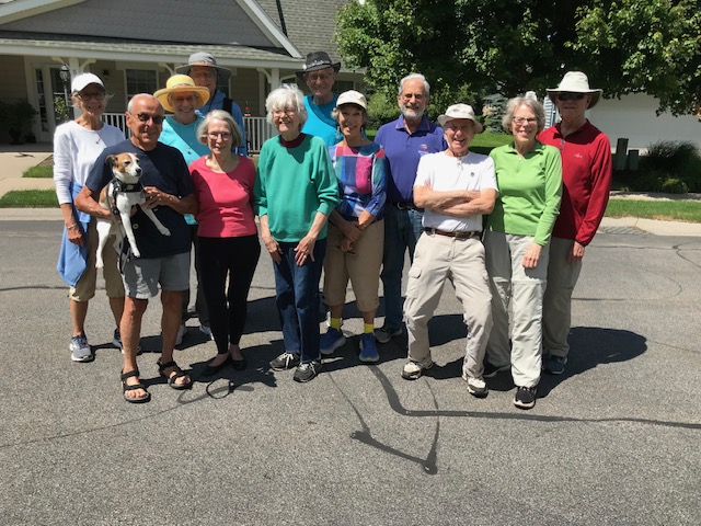 Members of The Highlanders Hiking Club pose for a group photo on a summer day in front of one of the Cottage Homes at The Highlands at Pittsford